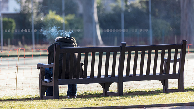 A photograph of a man sitting on a bench, smoking