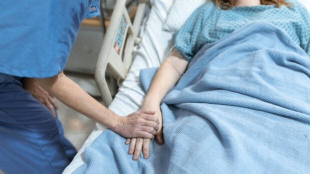 Clinician holds hand of patient on hospital bed.