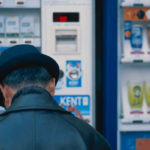 A photo of a person with their back to the camera, standing in front of a cigarette dispenser.
