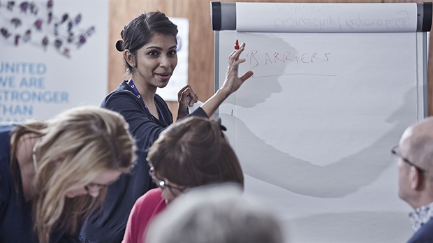 a woman holding a pen at a flip chart with the word 'barriers' written on it