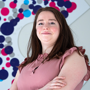 Picture of Dr Sorcha Hume standing in front of a cancer research uk logo