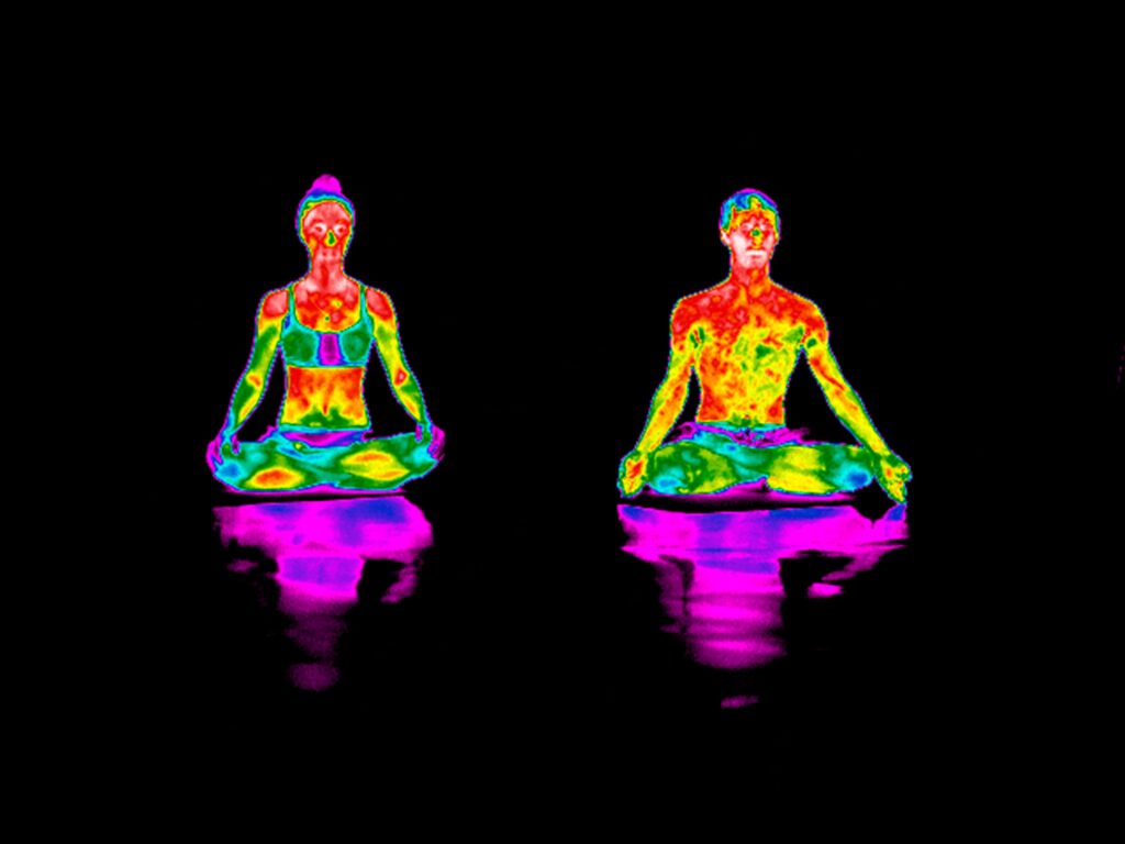 Two people practicing yoga, seen through a thermal camera.