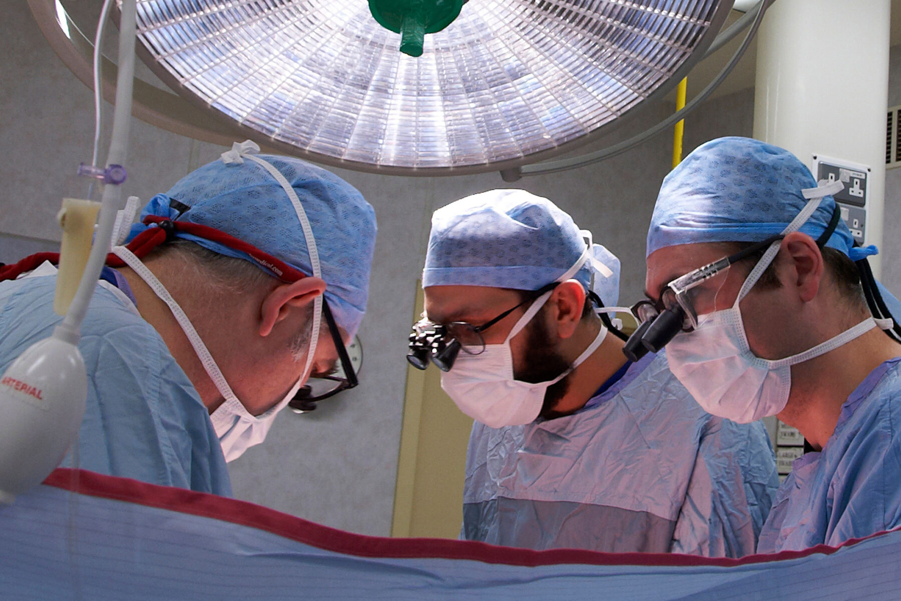 Three NHS surgeons operating under theatre lights.