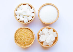 Four bowls containing brown, white, granulated and cubed sugar.