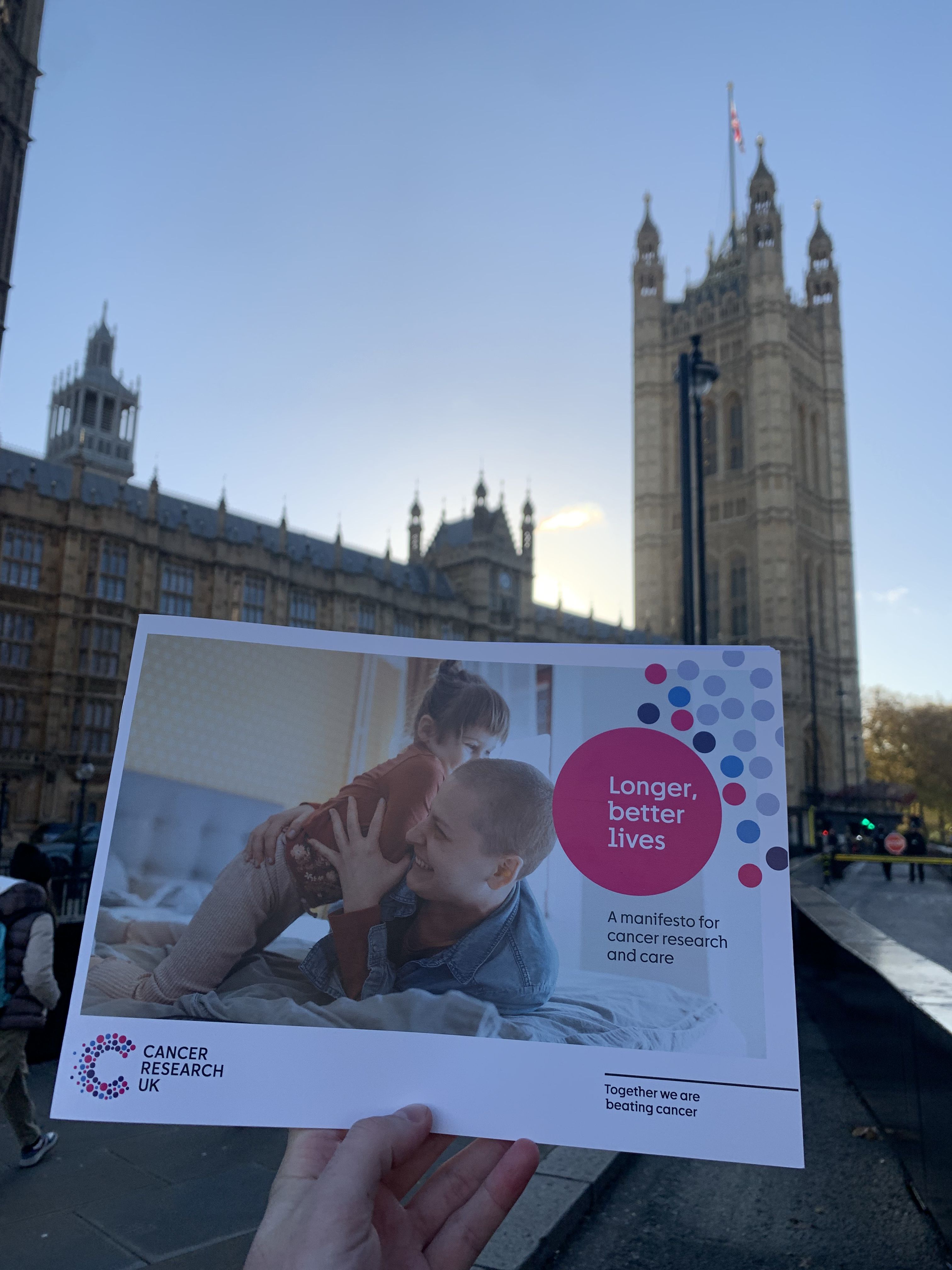 An image of Longer, better, lives: a manifesto for cancer research and care being held outside Westminster