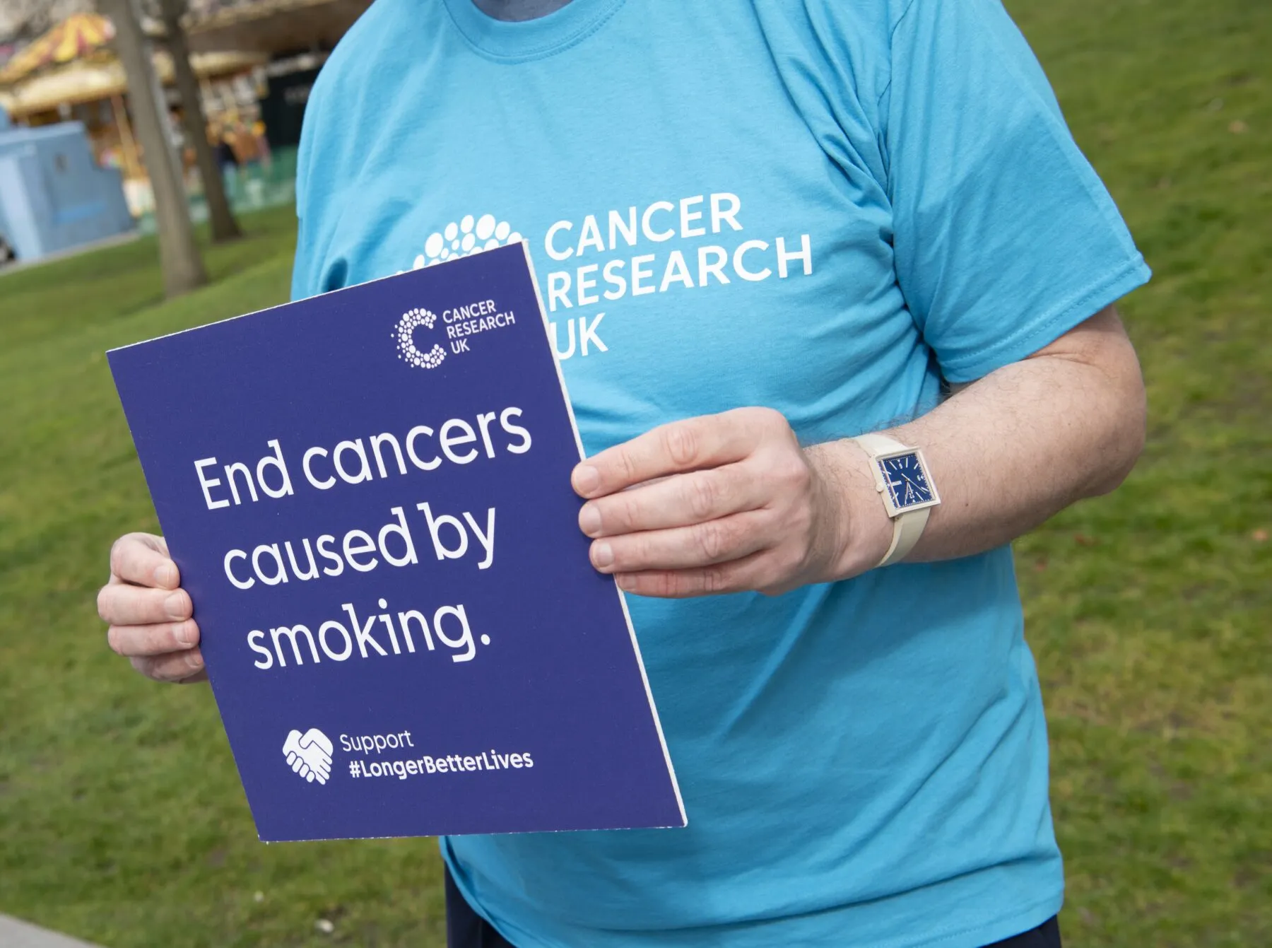 A campaigner in a Cancer Research UK t-shirt holding a sign that reads 'End cancers caused by smoking.'