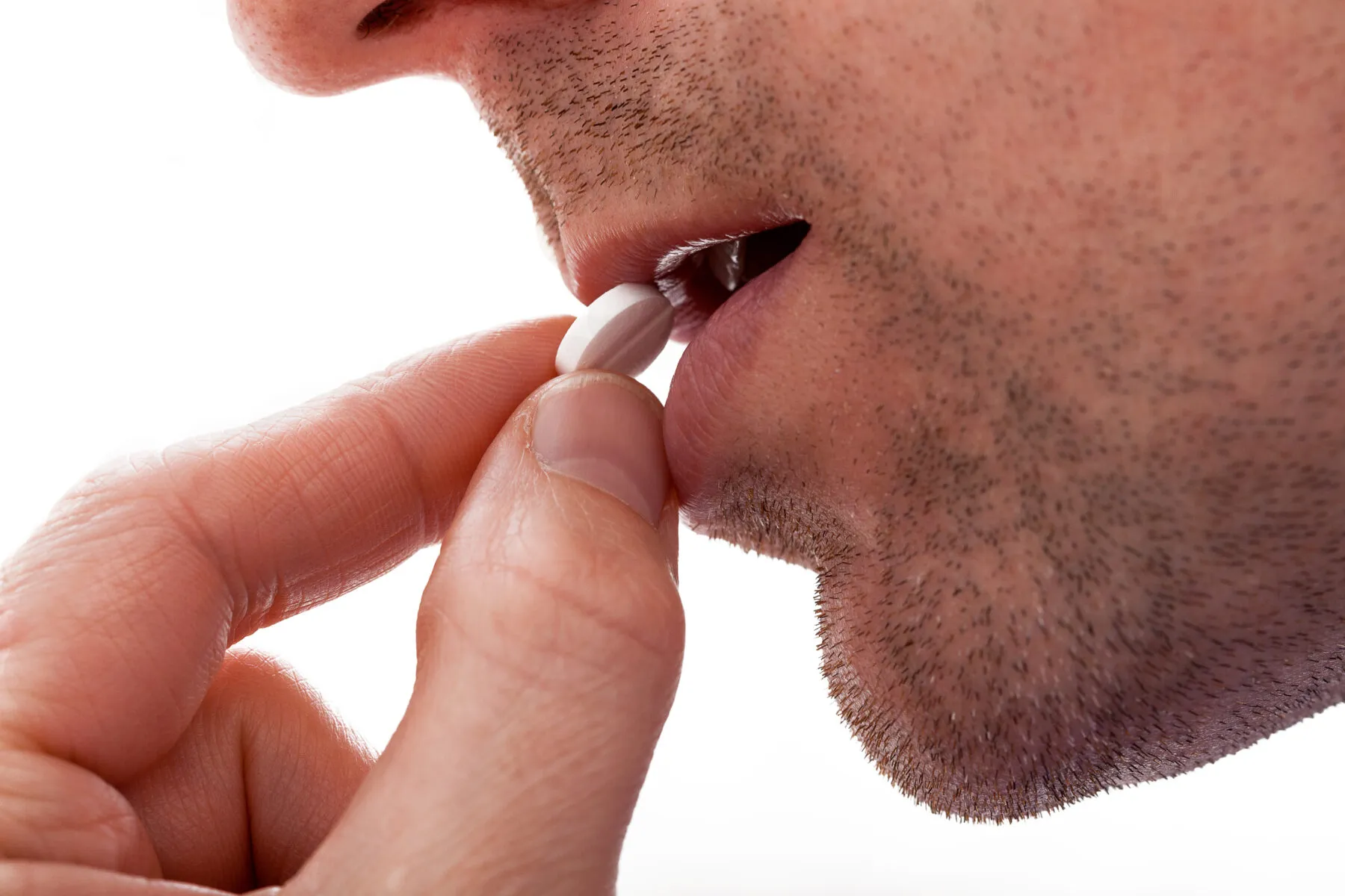 A close up of a man putting a pill into his mouth