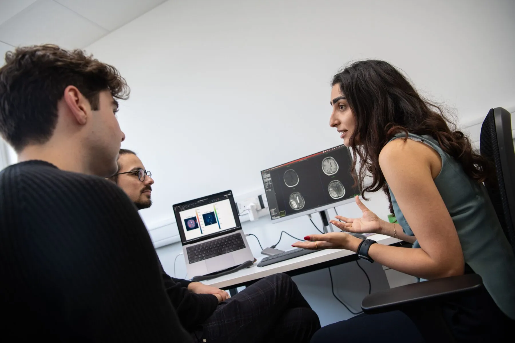 Three researchers discussing brain scans shown on a computer screen.