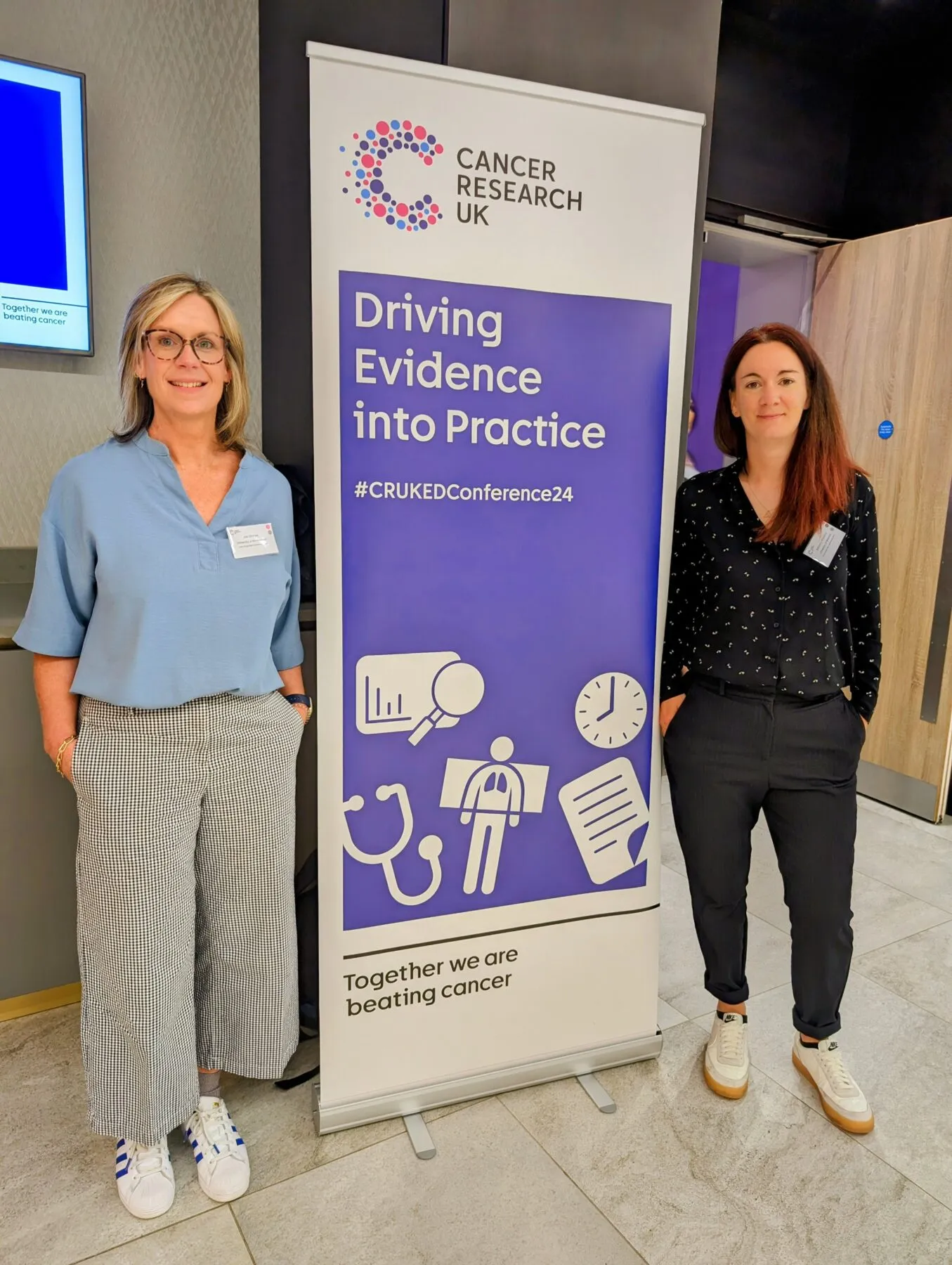 Dr Jacqueline Dinnes and Professor Bethany Shinkins next to a poster that reads 'Driving evidence into practice' at Cancer Research UK's 2024 Early Diagnosis Conference.