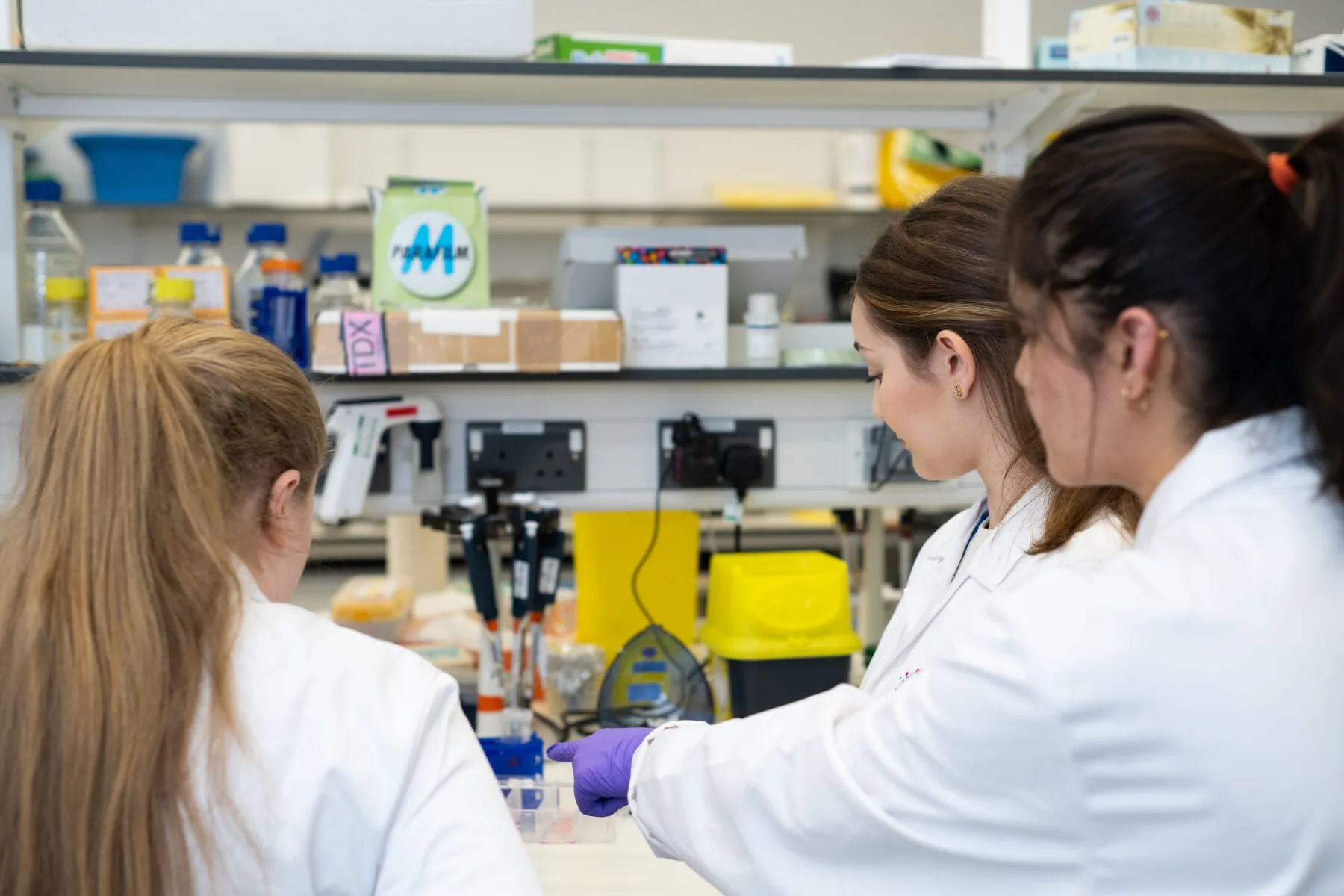 A group of three Cancer Research UK scientists Group of researchers pointing at something on a lab desk