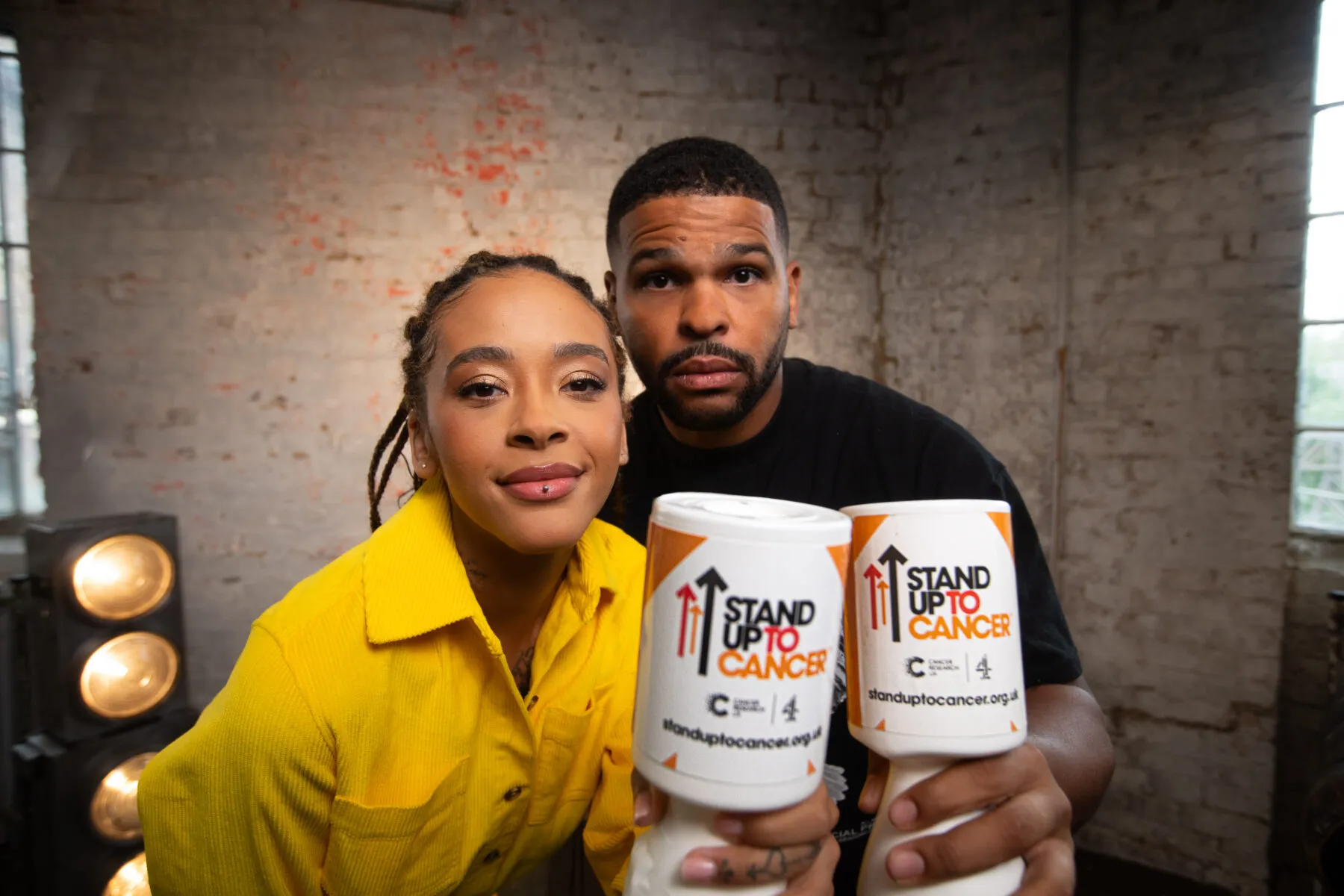 Yinka and Kola Bokinni holding Stand Up To Cancer donation jars