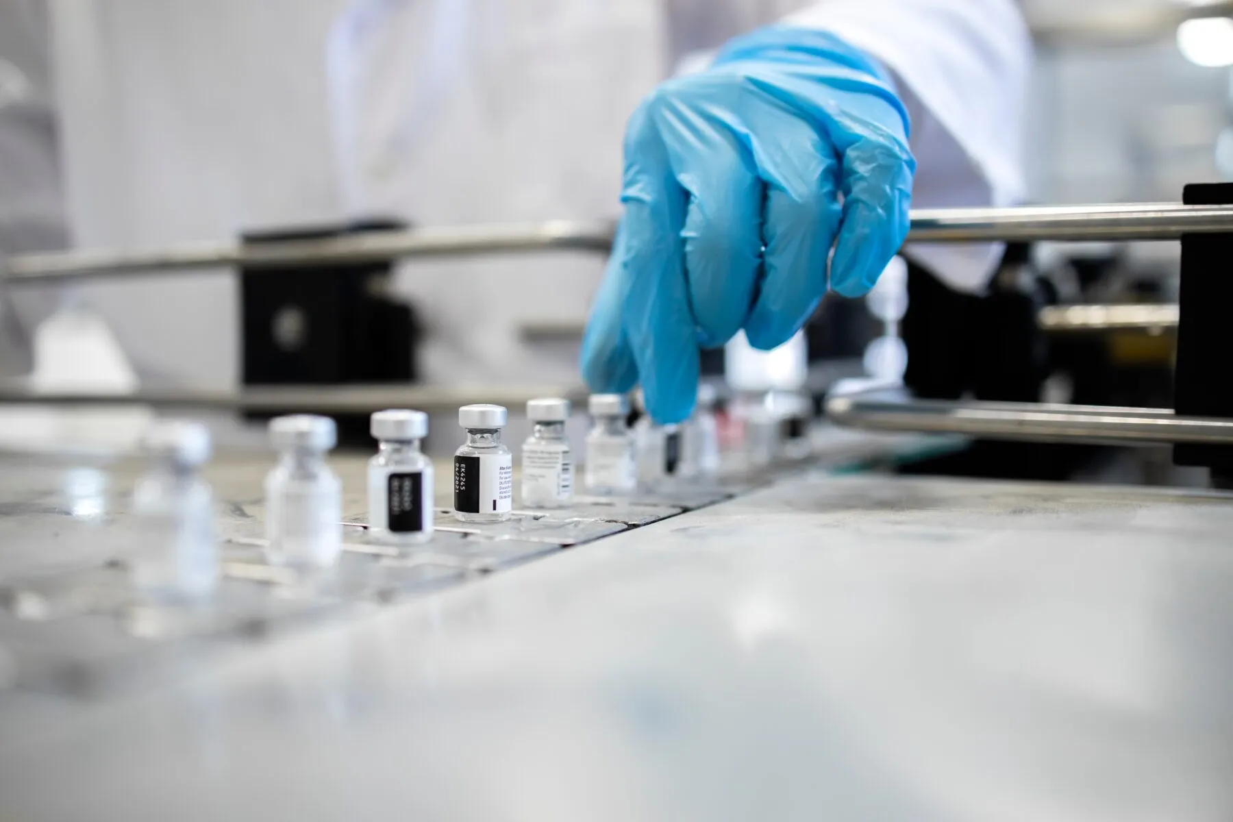 vaccine vials on a production line with a gloved hand reaching to grab one of them