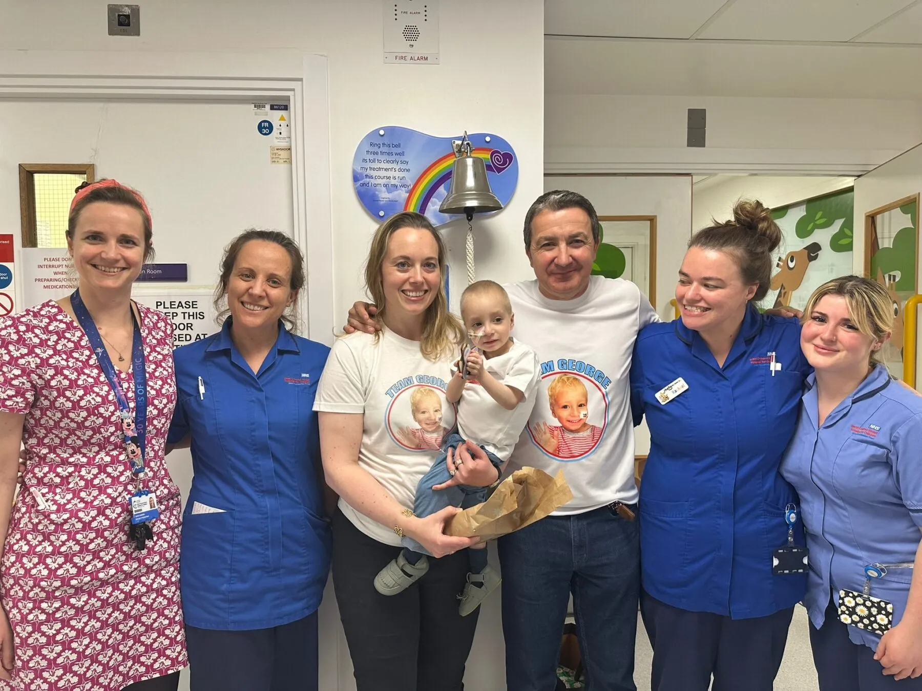 George and his parents stand by the bell in hospital surrounded by medical staff