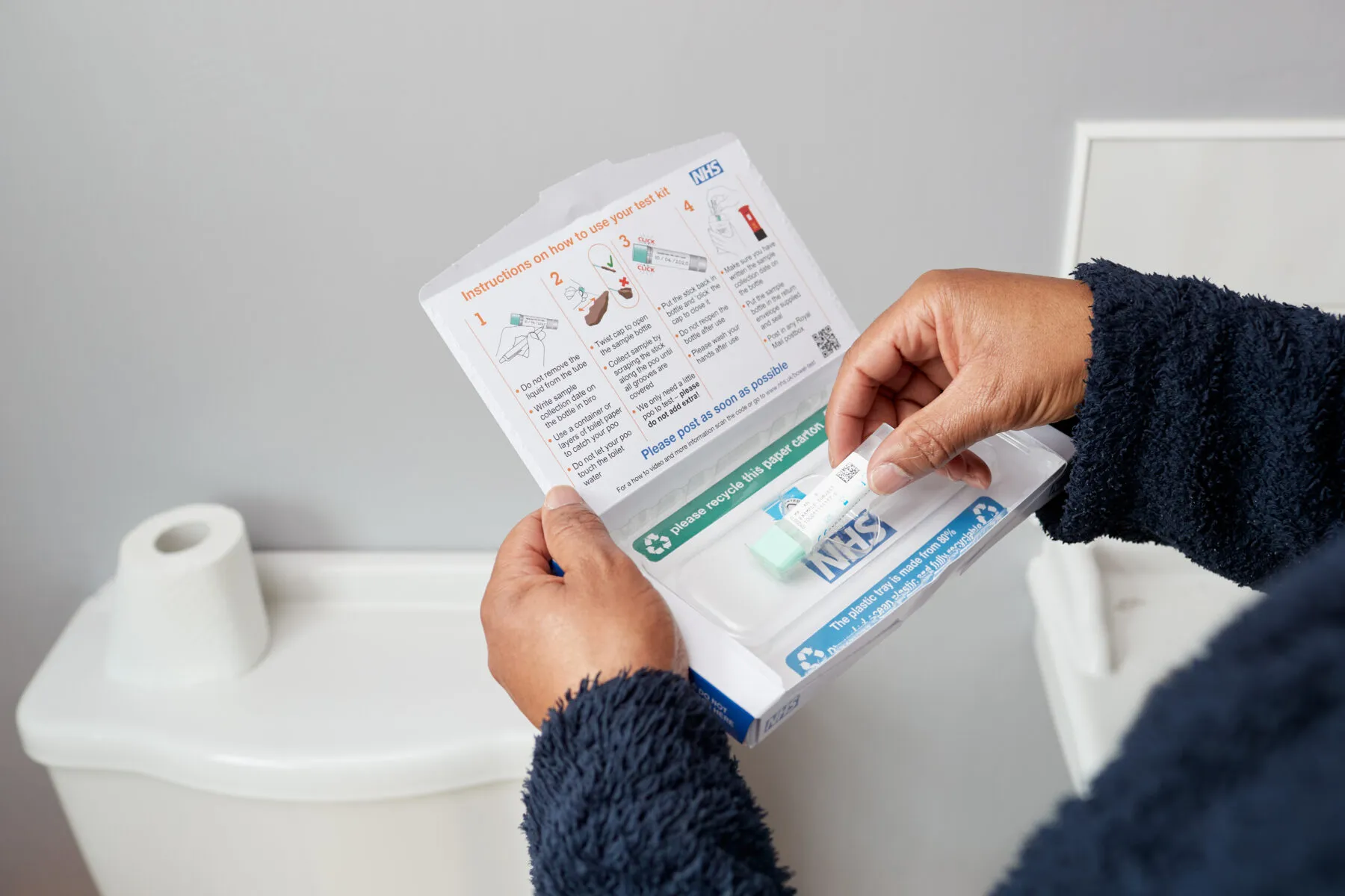 A man in a bathroom opening a bowel cancer screening test kit from NHS England.