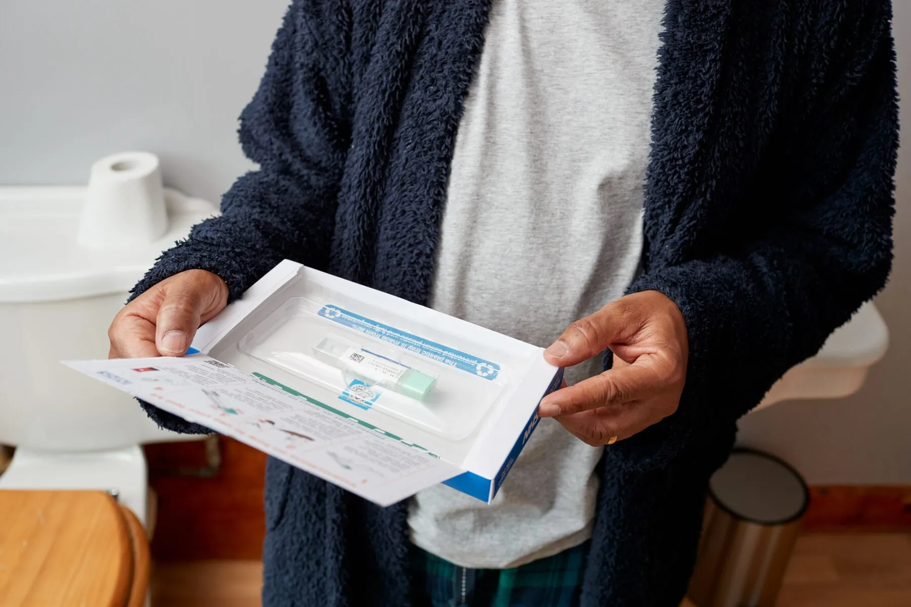 A man in a bathroom opening a bowel cancer screening test kit (FIT kit) from NHS England.