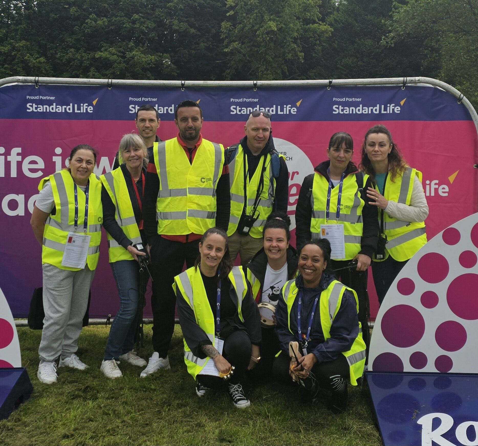 a group of 10 people wearing high vis jackets and standing in front of a Race for Life sign