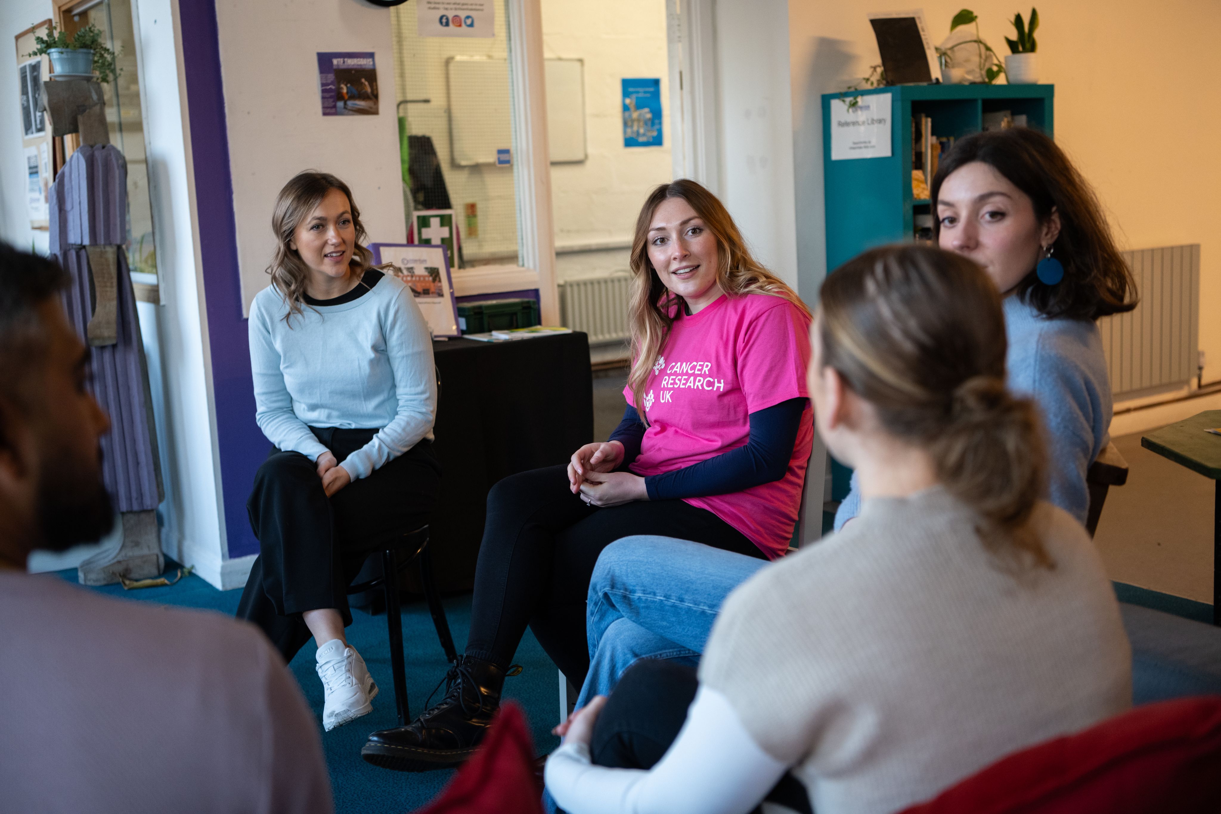 Volunteers, one wearing a pink Cancer Research UK branded tshirt, sitting in a circle and talking