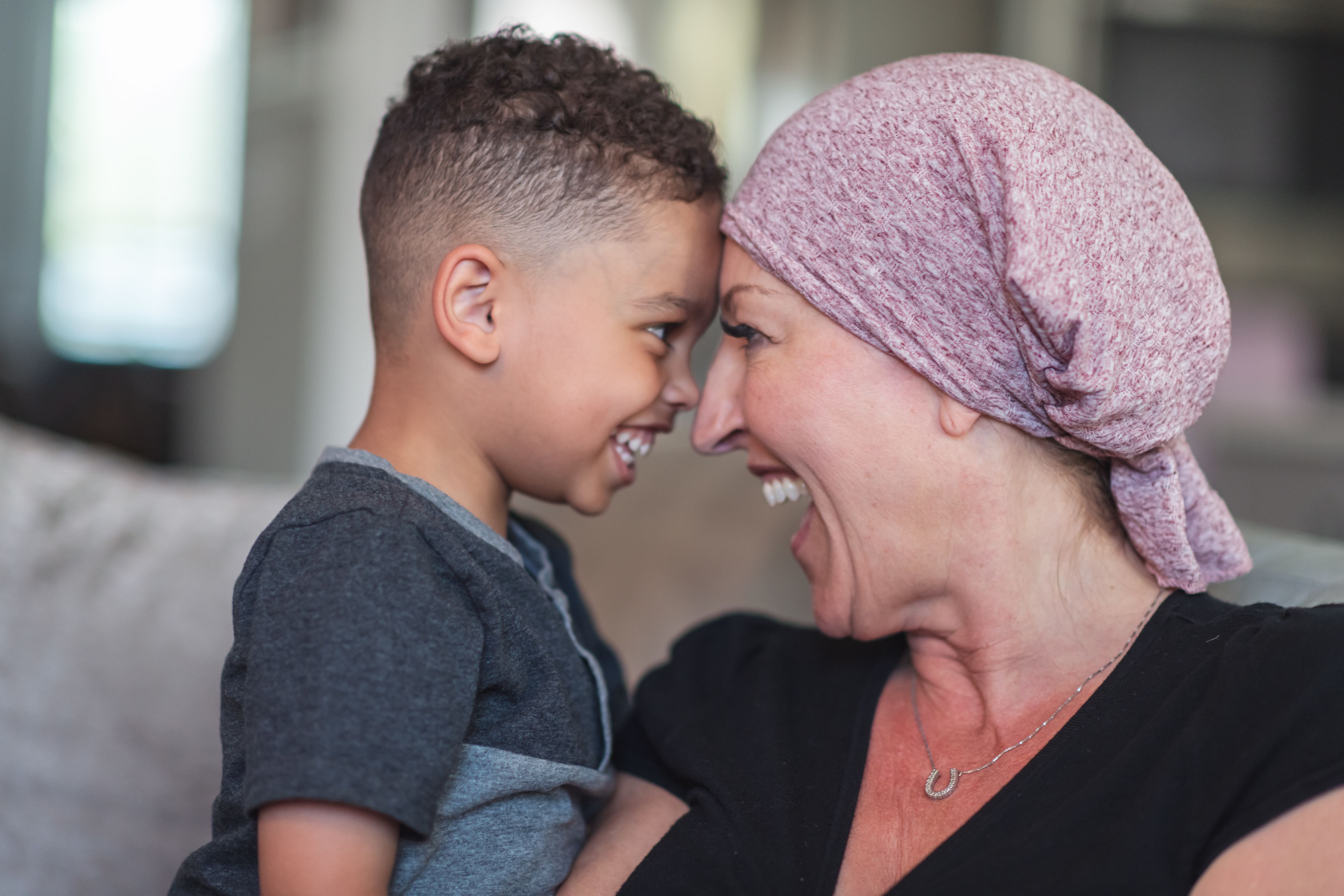 A child and a woman grinning at each other, their foreheads touching