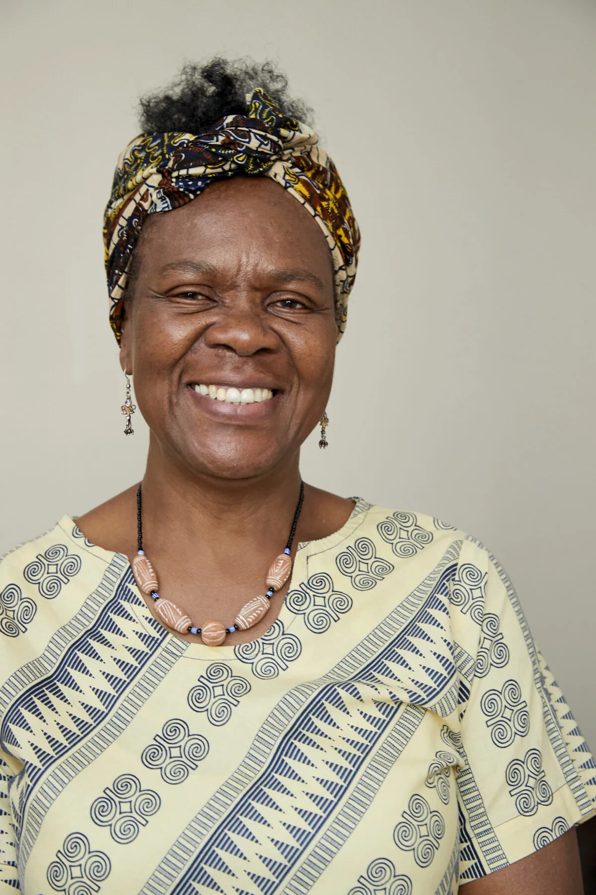 A head-and-shoulders image of Laurel smiling in her home. She is dressed in a yellow patterned top and an African-patterned headband.