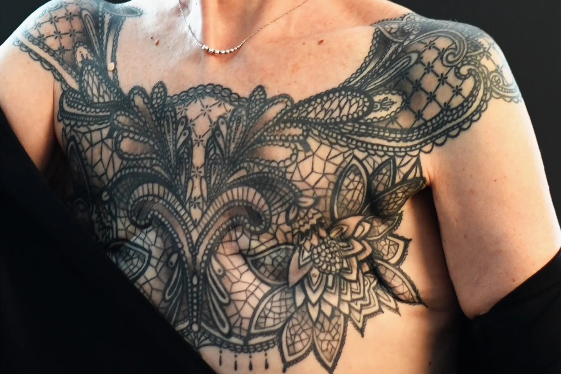 Sue's tattoo. A symmetrical black ink chest piece stretching up over her shoulders. Lacework connects a series of mandala patterns and lotus flowers.