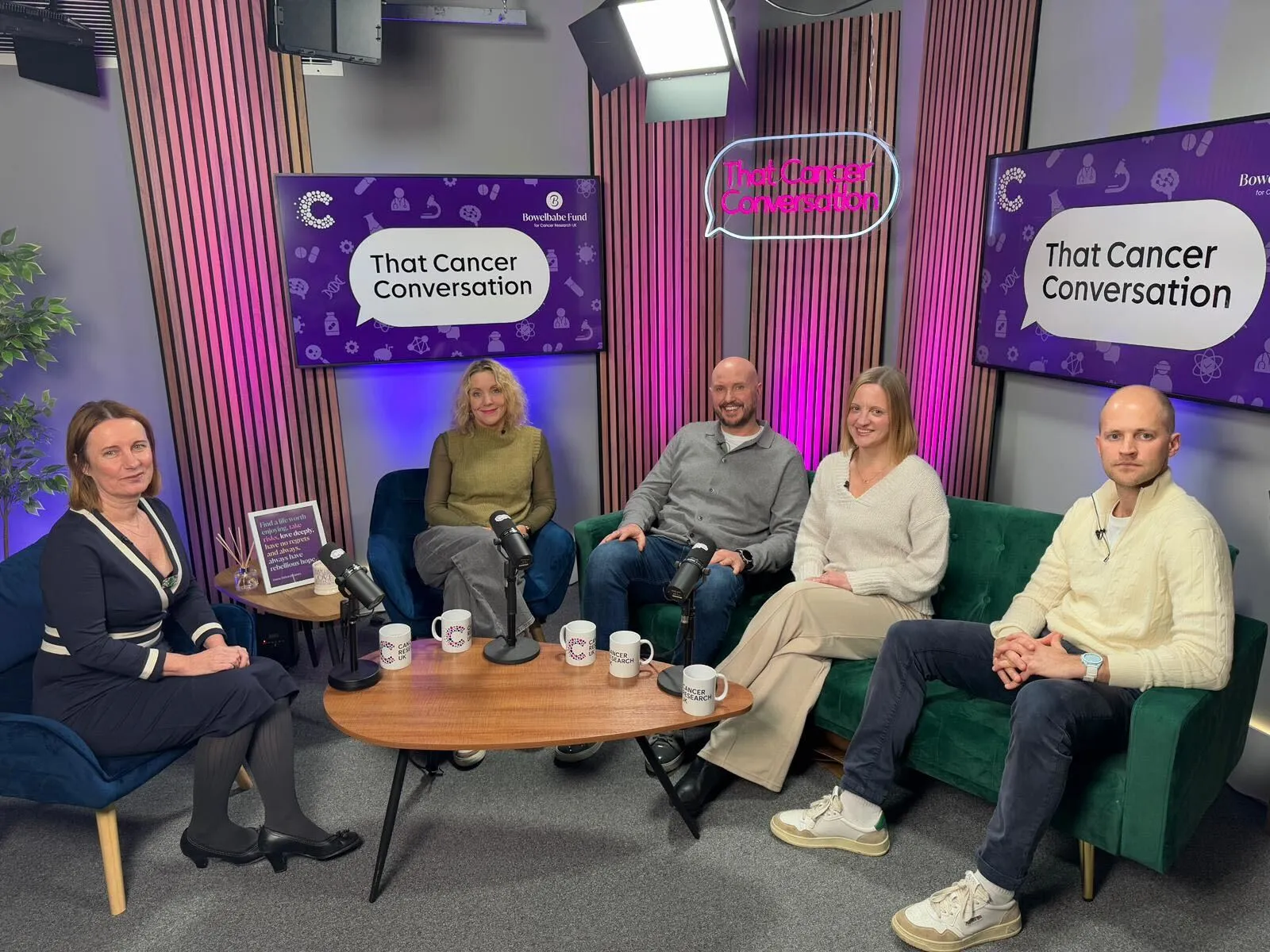 From left to right, Michelle Mitchell sitting in a chair followed by Emma Campbell, Steve Bland, Sarah Wieczorek and Ben James sitting on a couch in front of microphones in the podcast studio