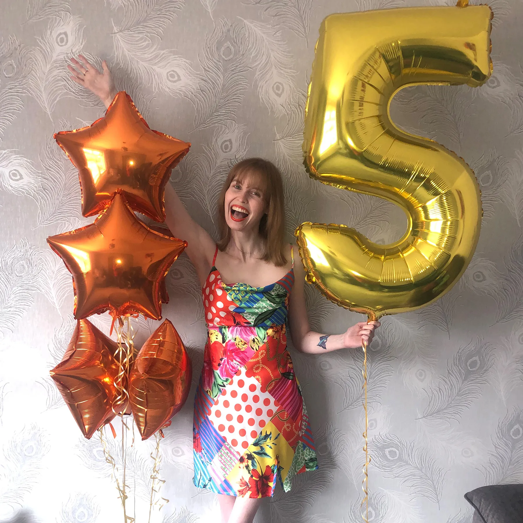 Eilidh celebrating the fifth anniversary of the end of her leukaemia treatment at home. She is wearing a summer dress with different colourful patterns and holding a balloon shaped like the number five.