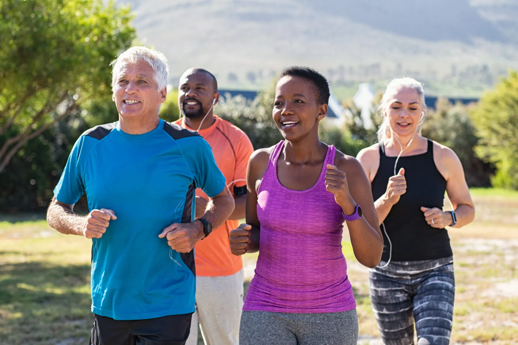 A group of four middle-aged adults jogging alongside a track in a park on a sunny day.