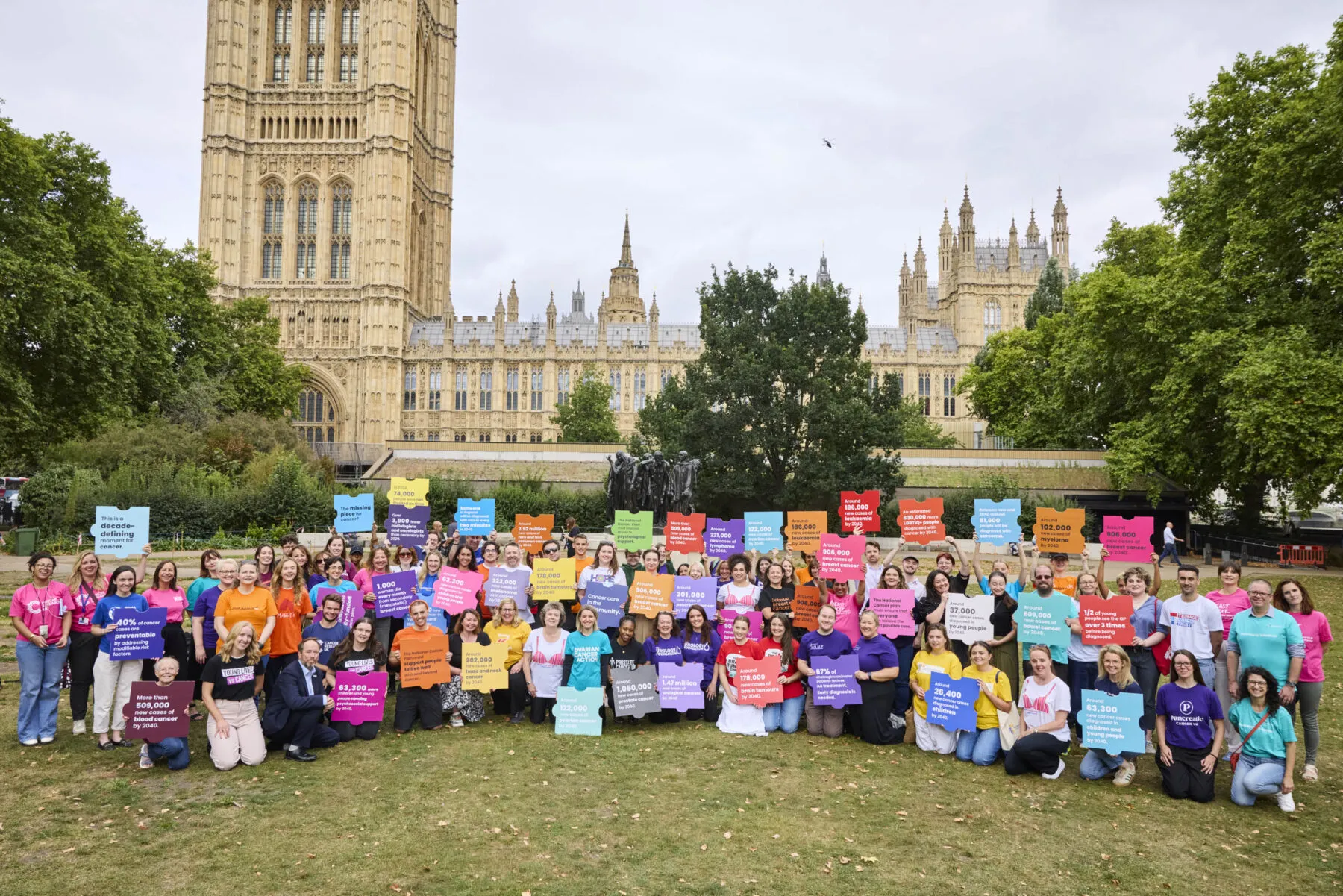 People in colourful T-shirts holding up puzzle pieces gather outside Parliament.