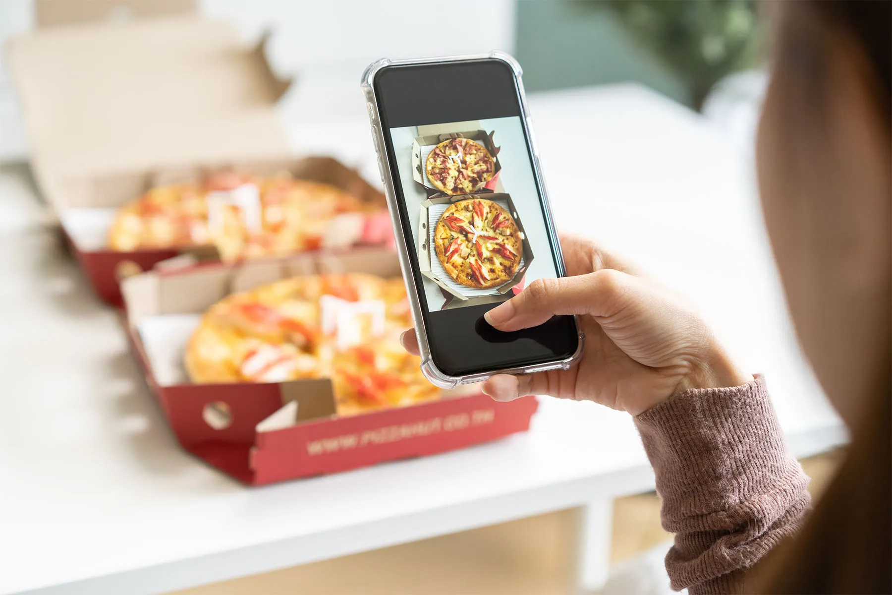 A person using a smartphone to take a picture of two pizzas in takeaway boxes.
