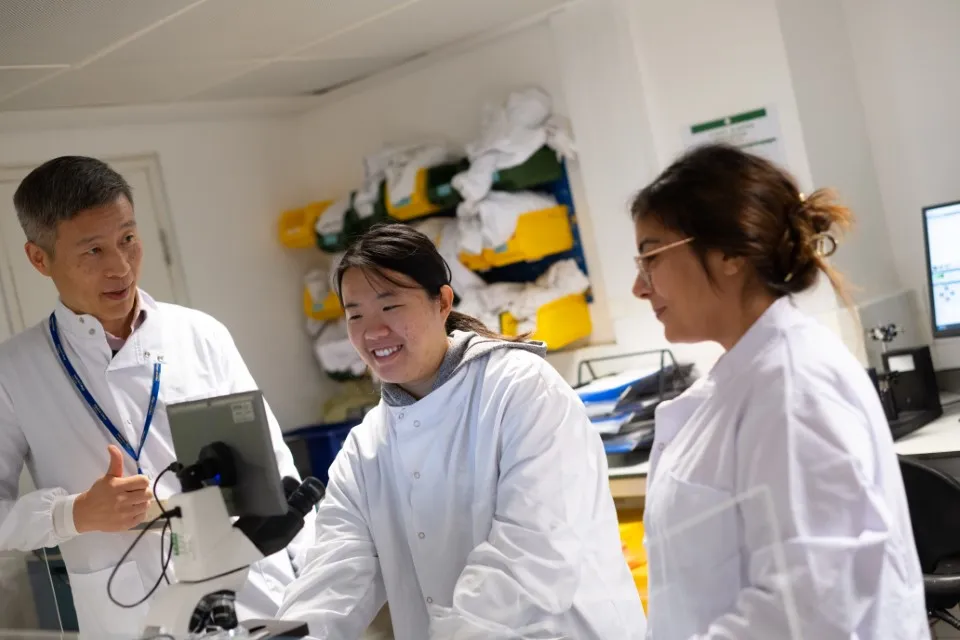 Three researchers at a lab bench. They are wearing white lab coats.
