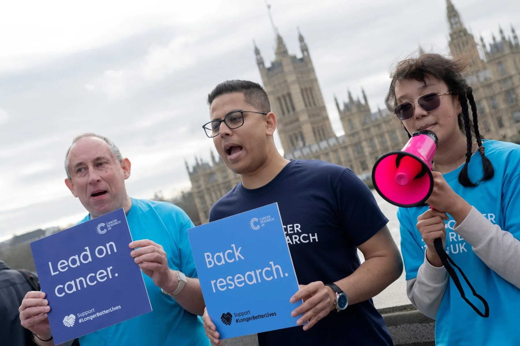 Campaigners holding signs opposite the Houses of Parliament in London. The sign in the middle reads 'Back Research'.