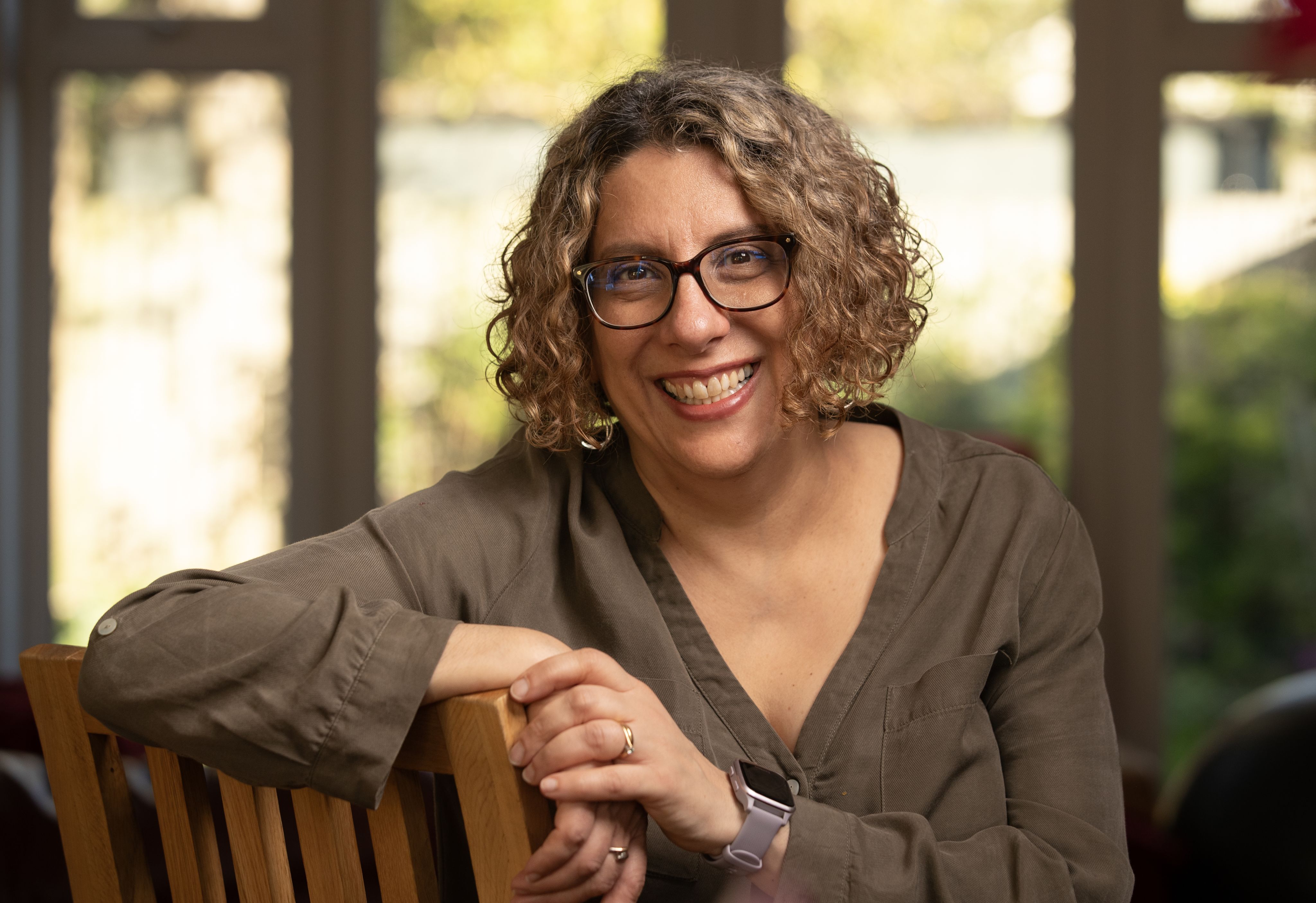 Lucy sat on a chair at home in a professional photograph. She's smiling at the camera.