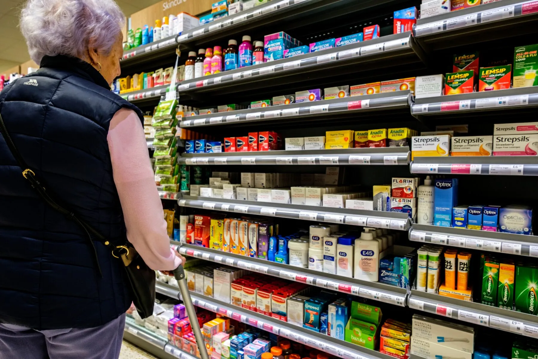 A woman facing away from the camera looks at medicine on pharmacy shelves.