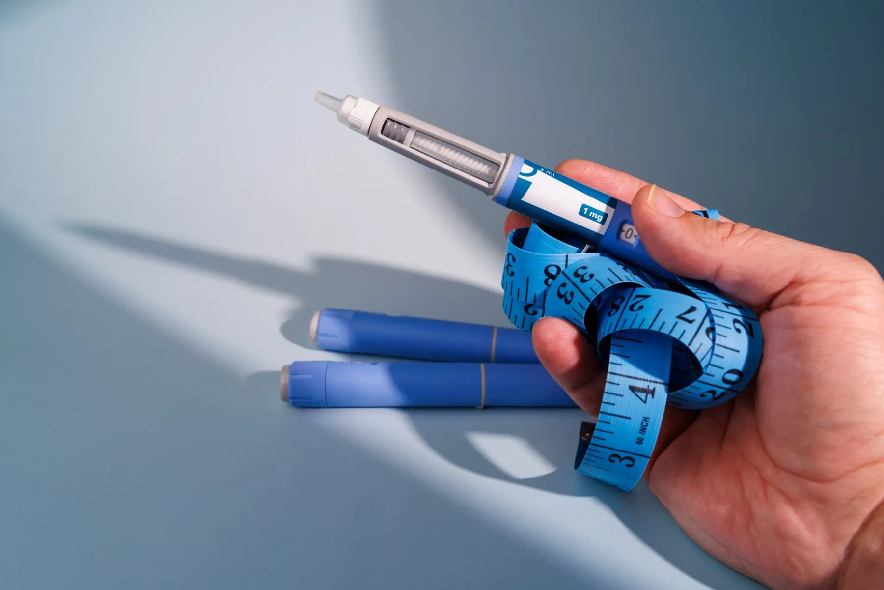 Patient hand holding injectable pens and measuring tape