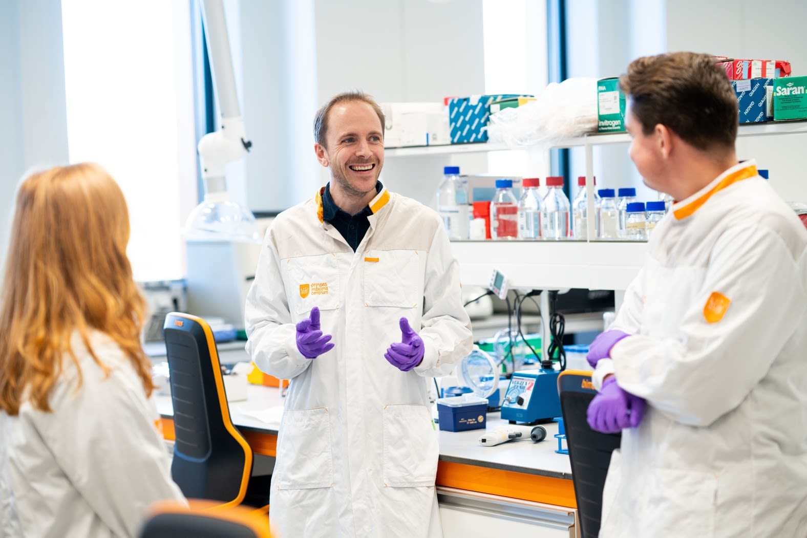 Three people in lab coats having a discussion in a modern research lab.