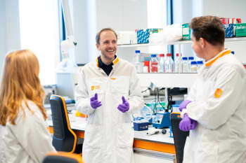 Three people in lab coats having a discussion in a modern research lab.