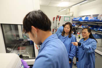 Three people in blue lab coats working with a sample processing machine in a lab.