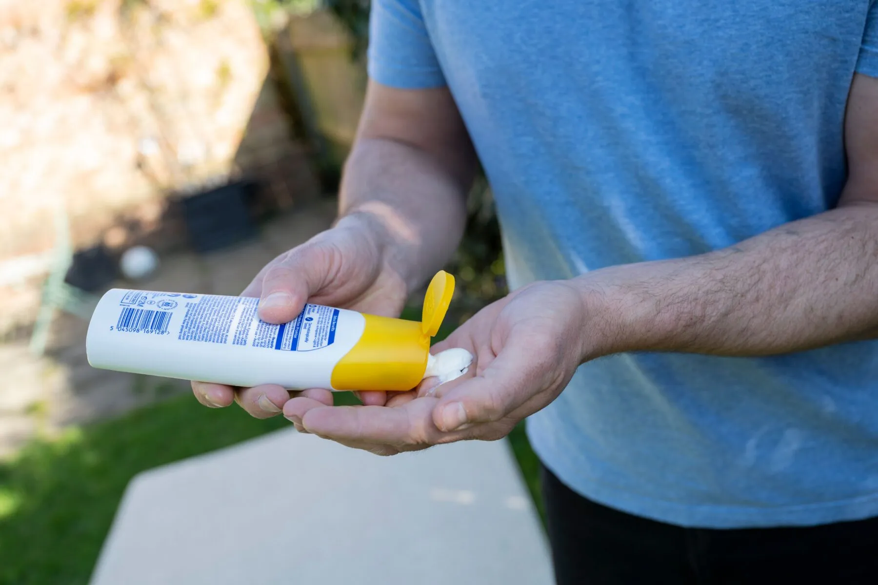 An man in a blue shirt and jeans applying squeezing sunscreen into his hand from a bottle.