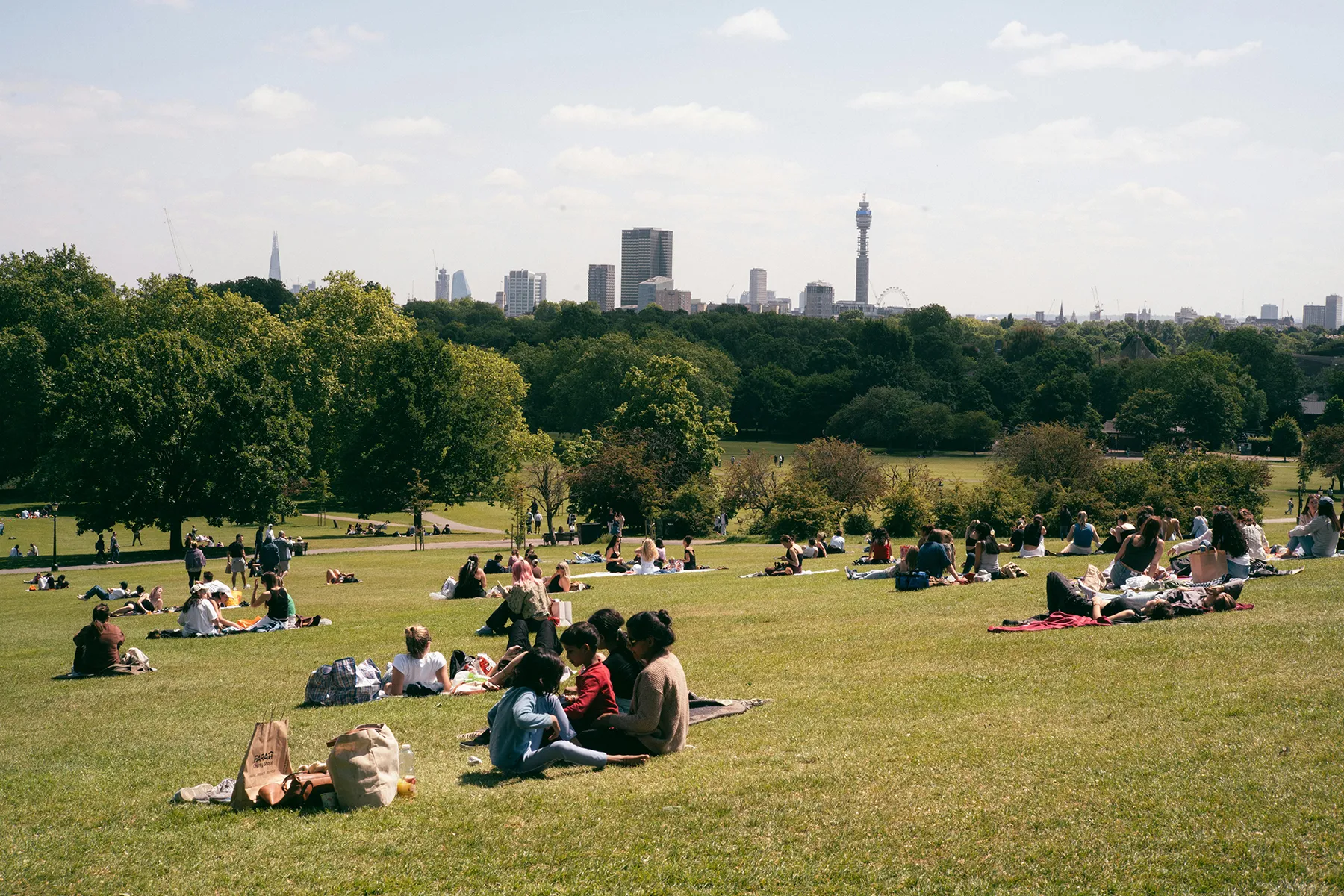 groups of people sitting on grass at park, London skylines in background