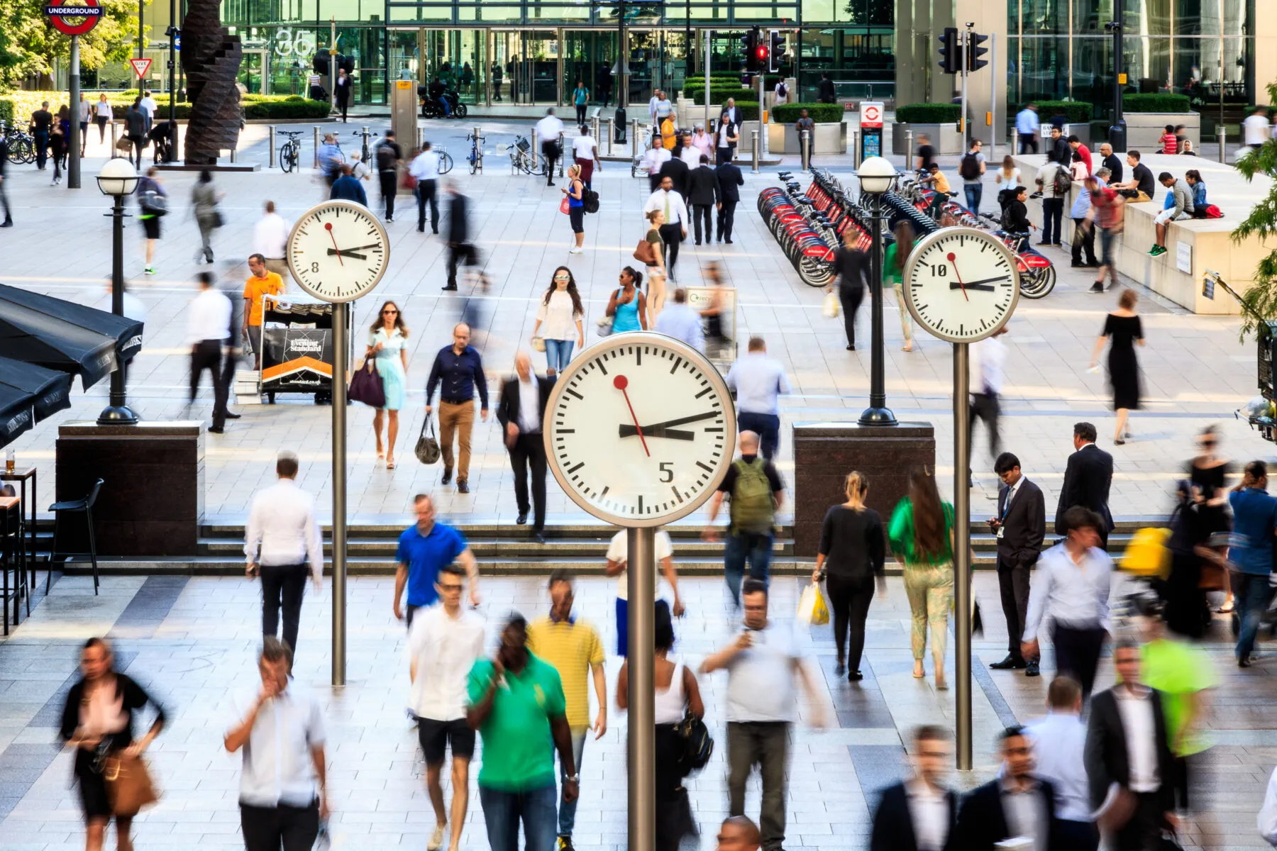 three silver clocks in an open space with people walking passed