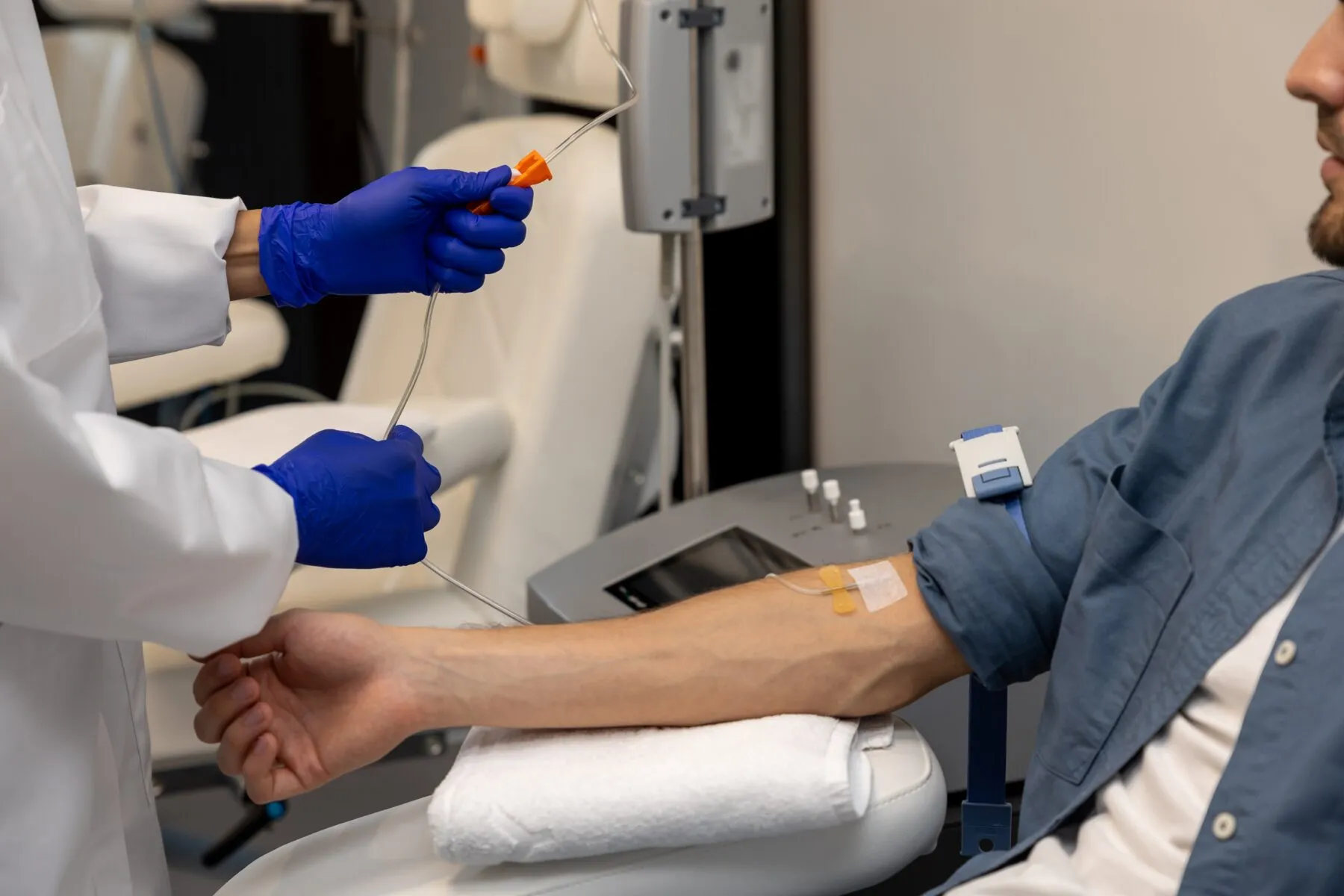 Man in blue shirt seated with an IV in his arm next to a clinician adjusting IV drip