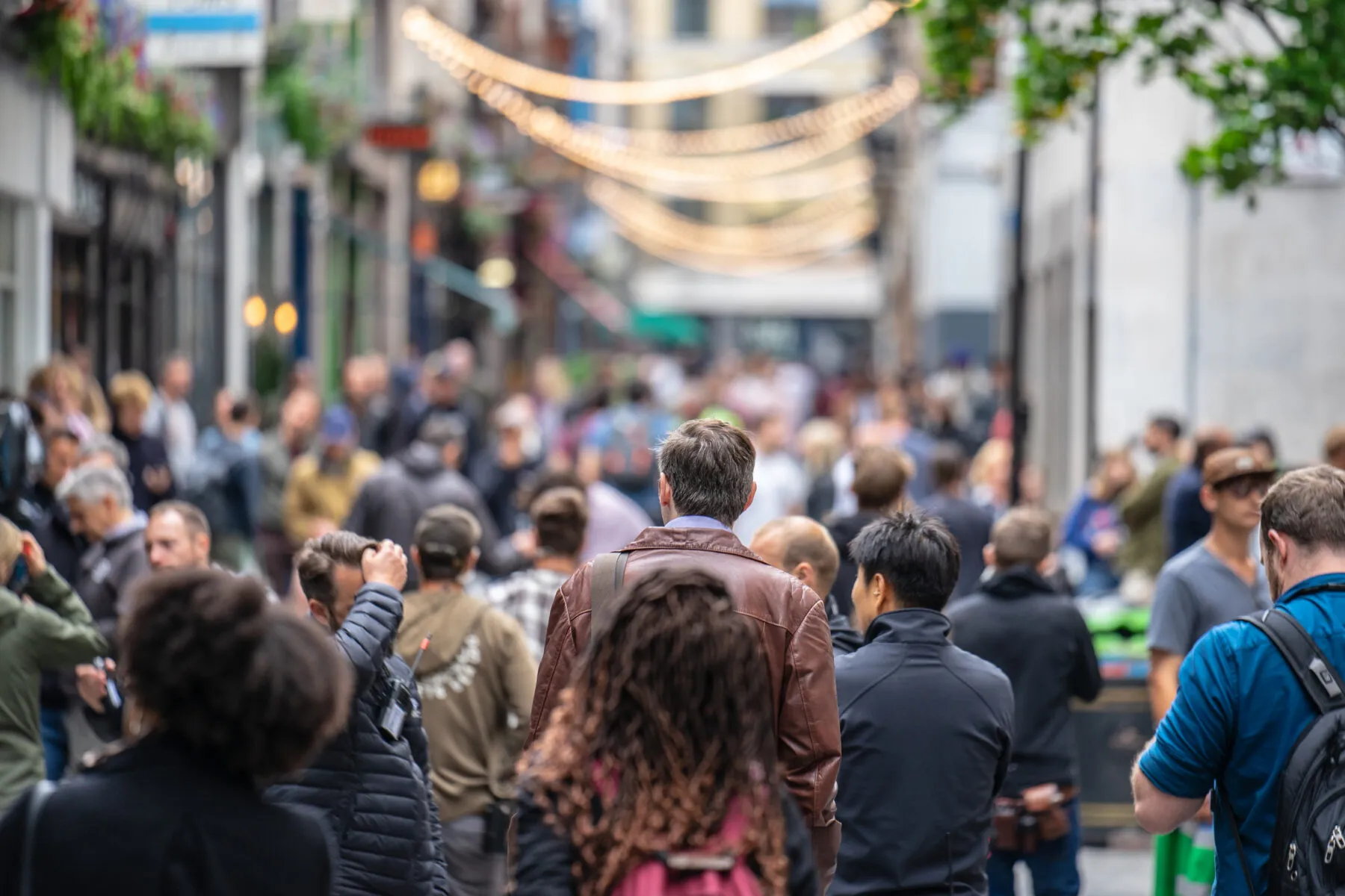 A crowd of people walking away from the camera down a busy street